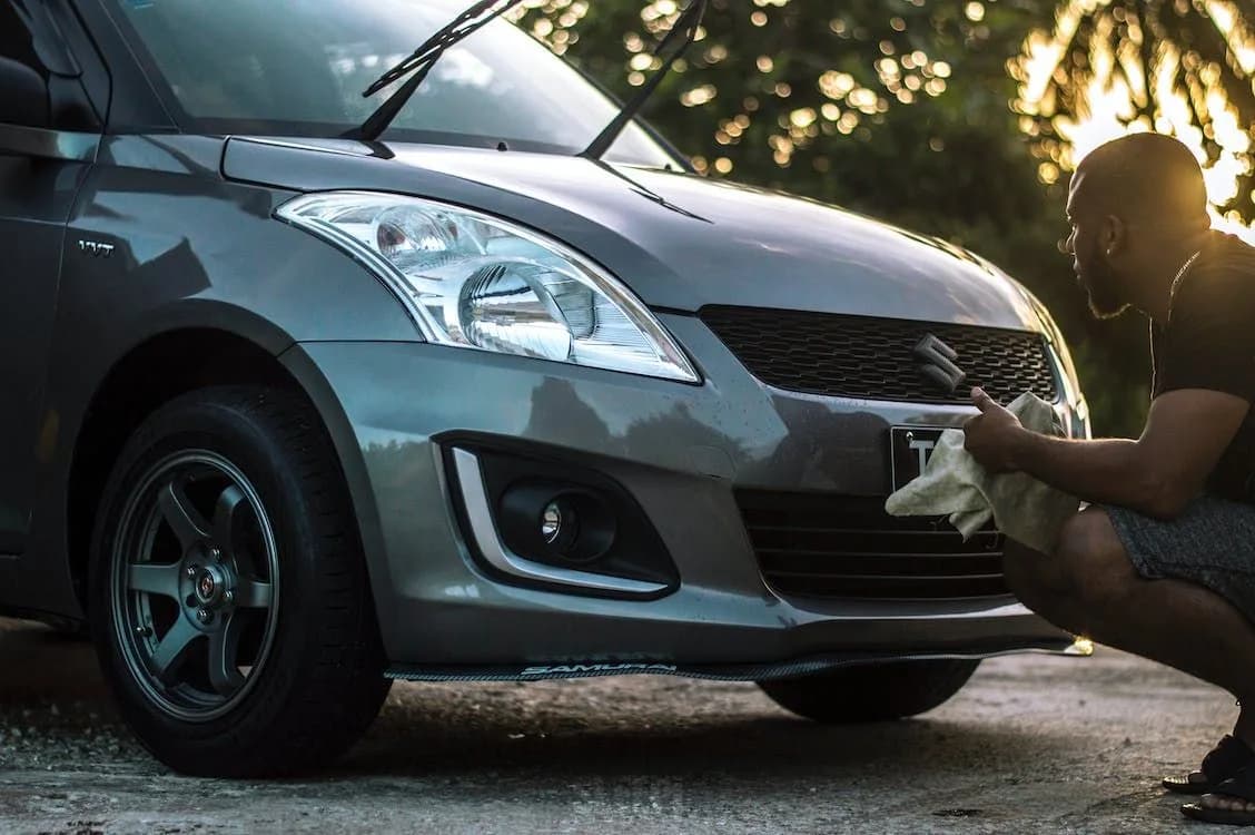 Persona limpiando el frente de un auto gris