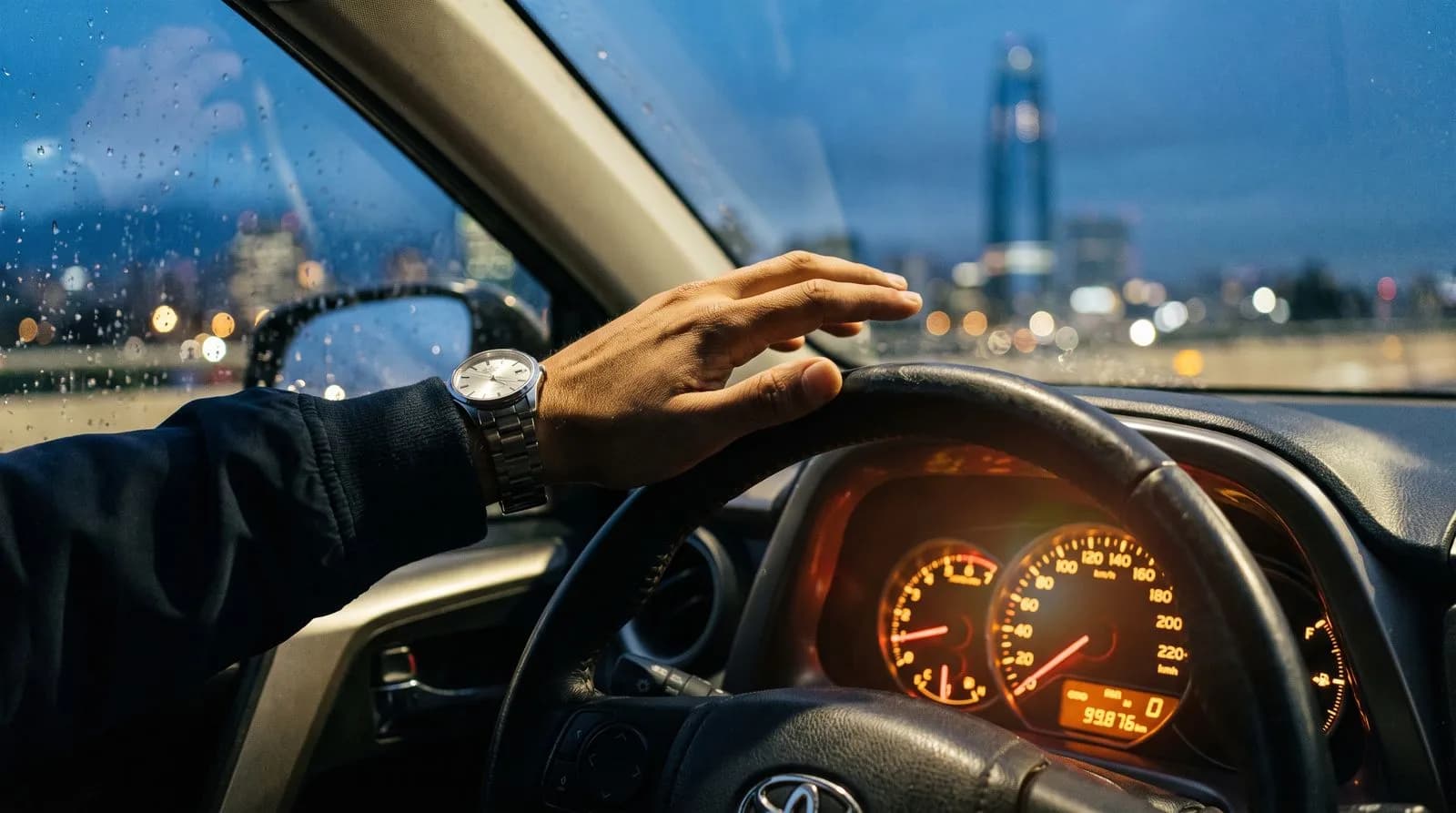 Manos al volante con el tablero encendido y la ciudad de fondo